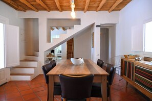 Uma sala de jantar com mesa de madeira, cadeiras pretas e escada que leva a outro cômodo.
