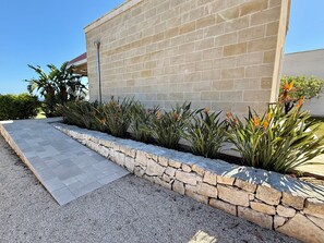 Un bâtiment moderne doté d’un mur de soutènement en pierre, d’un chemin piétonnier pavé et de plantes ornementales.