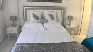 Een netjes opgemaakte slaapkamer met een groot bed, twee nachtkastjes en een kunstwerk aan de muur boven het bed.