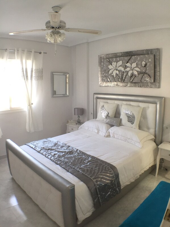 A bedroom with a bed, a ceiling fan, a nightstand, a lamp, and a painting on the wall.