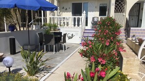 Een terras met buitenmeubilair, plantenpotten en een blauwe parasol.