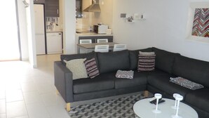 En moderne stue med en hjørnesofa, et rundt sofabord og et mønstret tæppe.