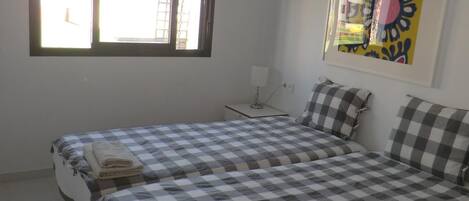 A room with two beds, a window, a bedside table, and a wall-mounted artwork.
