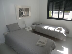 Une chambre avec deux lits, une table de chevet, une lampe et une fenêtre avec des stores.