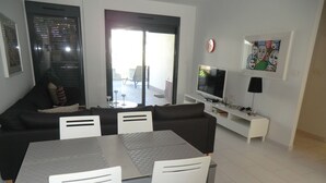 En moderne stue med en sort sofa, hvide stole, et spisebord, et fjernsyn og et billede på væggen.