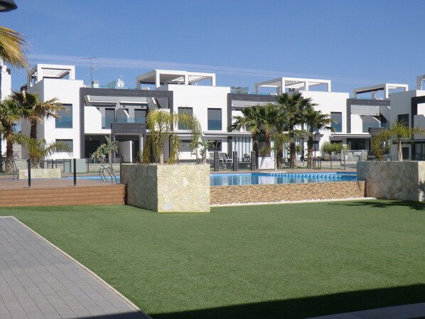 Un hôtel moderne doté d’une piscine, de palmiers et surplombant un ciel d’un bleu limpide.
