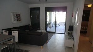 En moderne stue med sofa, spisebord og stole. Der er en skydedør, som fører til en udendørs terrasse.