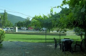 A patio area with a table and chairs, a hose, and a view of parked cars and a hill in the background.