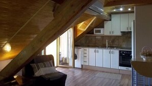 A loft-style living area with a sloped ceiling, wooden beams, a sofa, and a kitchen with white cabinets and a microwave. - Maribel Tourist Apartment for 5 people (Biescas)