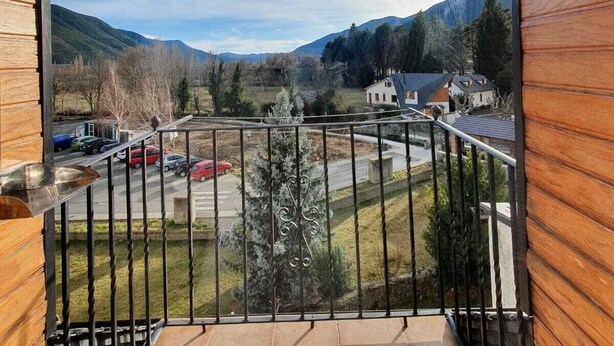 A wooden balcony with a metal railing overlooking a parking lot and a residential area with houses and trees. - Maribel Tourist Apartment for 5 people (Biescas)
