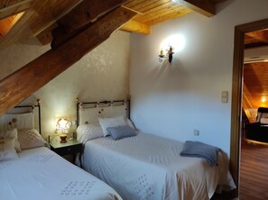 A cozy attic bedroom with two beds, a wooden ceiling, and a small table with a lamp.