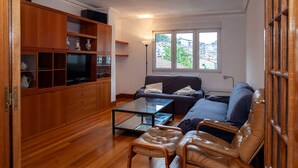 A living room with a sofa, leather chairs, a glass coffee table, wooden cabinets, and a view of buildings through a window. - FLAT in the CENTER OF ONDARROA, fishing village, with WIFI 600MB, without slopes. (ONDARROA)