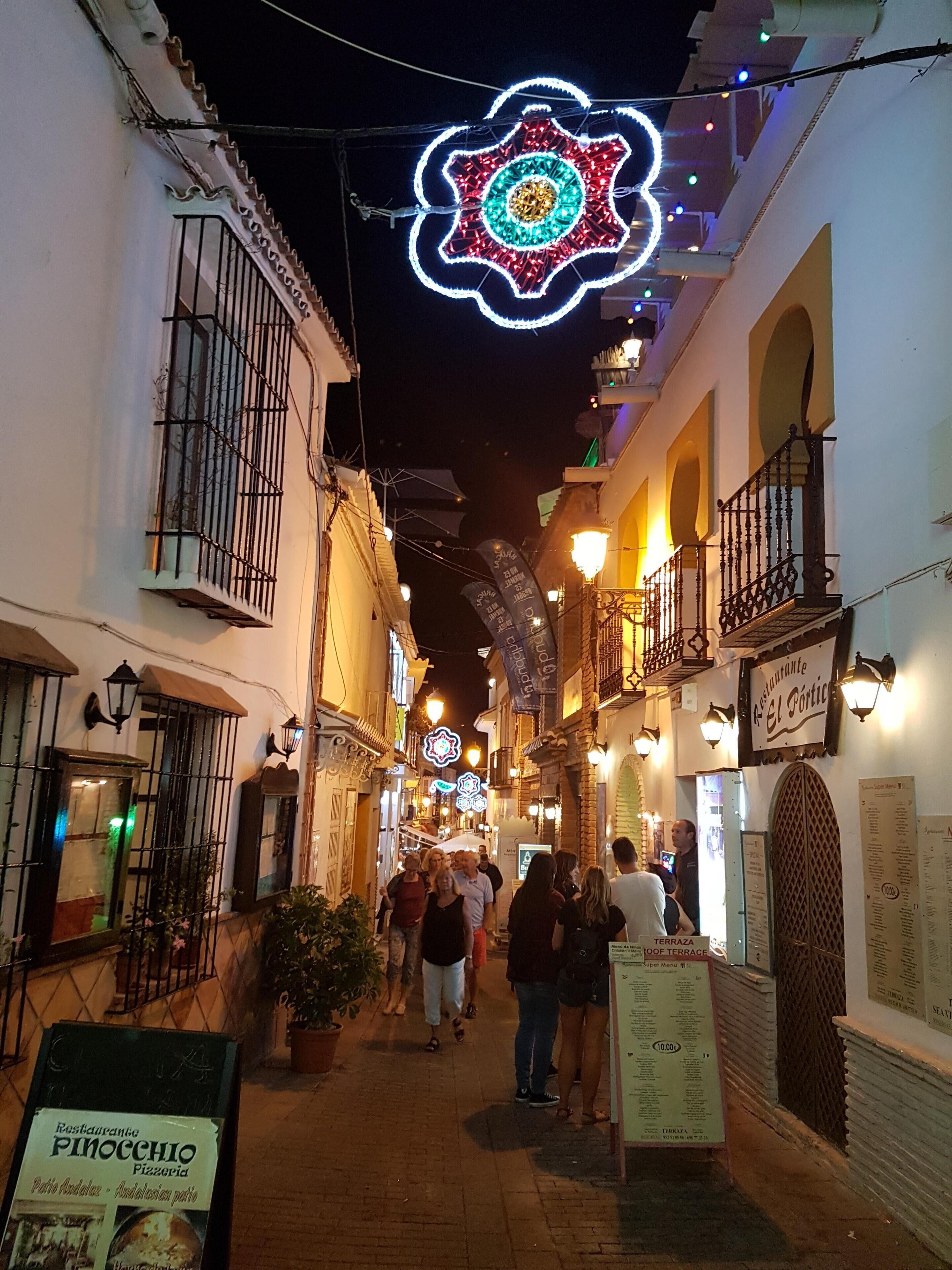 Un estrecho callejón flanqueado por edificios, iluminado con luces de cadena y decorativas.
