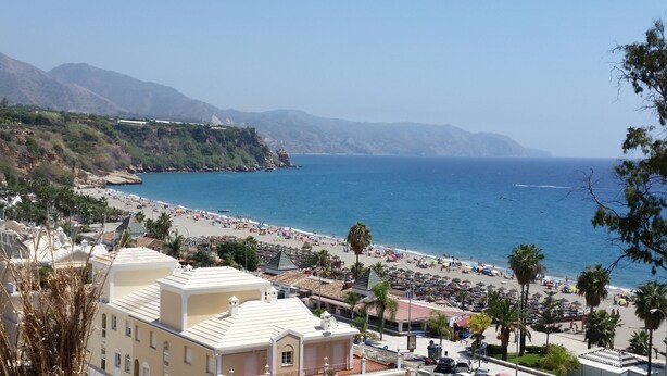 A coastal town with a beach, buildings, and mountains in the background.