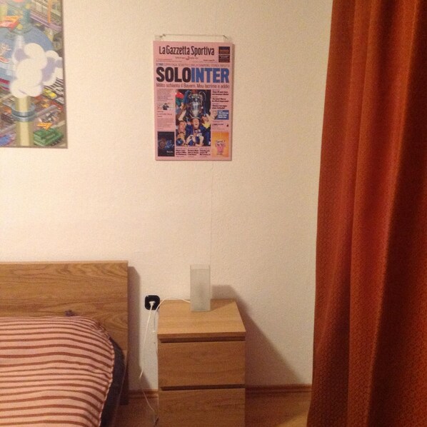 A bedroom with a bed, a nightstand with a lamp, and a poster on the wall.