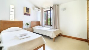 Ein Schlafzimmer mit zwei Betten, einem Fenster mit Vorhängen, einem Nachttisch mit einer Vase und einer Klimaanlage.