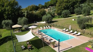 Et rektangulært swimmingpool med flisebelagt solterrasse, omgivet af liggestole og parasoller.