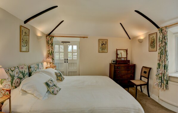 A bedroom with a large bed, a dresser, a chair, and a door leading to another room.