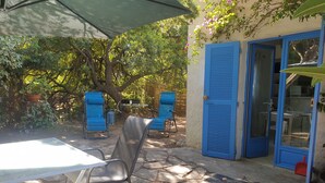 Een terras met stenen vloer, twee blauwe stoelen, een tafel en een blauwe deur.
