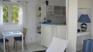 Een compacte keuken met witte kastjes, een eettafel met stoelen en een klein raam.