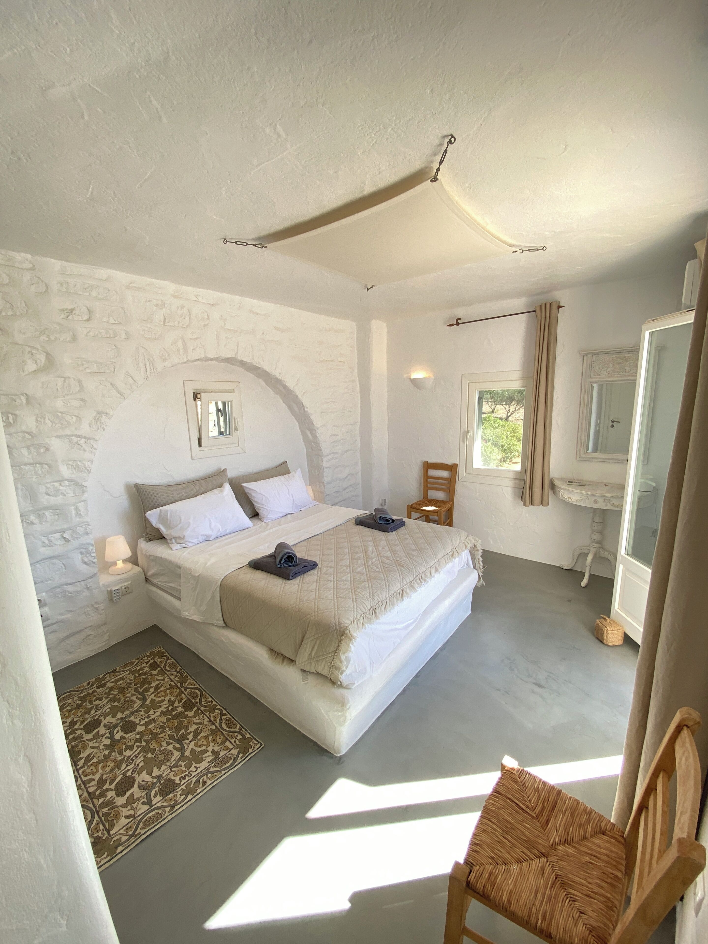 Un dormitorio con una cama grande, una mesita, una silla y una ventana.