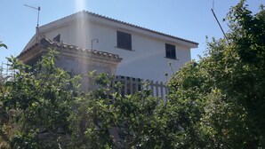 Un edificio de dos pisos con fachada blanca, techo de tejas y cerca de piquetes blancos.