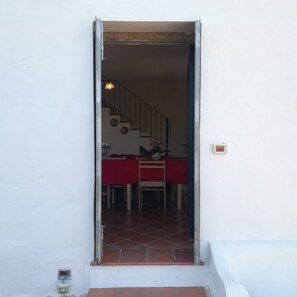 A doorway leading to a dining area with a red tablecloth, a staircase, and a wall-mounted light fixture.