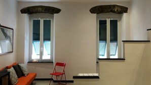 Una sala de estar moderna con un sofá, una silla plegable roja y dos ventanas con persianas.