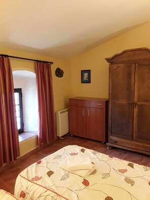 Une chambre à coucher avec un lit, une armoire, un radiateur et une fenêtre avec des rideaux.