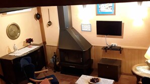 A cozy living room with a sofa, a table with a bowl of fruit, a fireplace, a television, and a small desk with a chair. - Casas Rurales Los Arrayanes for 4 people (Ronda)