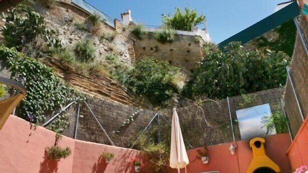 A patio with two chairs, a table, and a potted plant. There is a stone wall and a small garden area with plants. - Casas Rurales Los Arrayanes for 4 people (Ronda)
