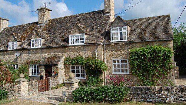 A stone cottage with multiple chimneys, white-framed windows, and a stone wall surrounding the property. - COTSWOLD COTTAGE IN A QUIET VILLAGE WITH LARGE GARDEN (Great Rissington)