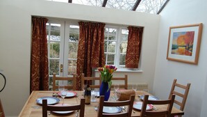 A dining room with a table set for four, a vase with flowers, and a window with curtains. - COTSWOLD COTTAGE IN A QUIET VILLAGE WITH LARGE GARDEN (Great Rissington)