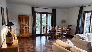 Uma sala de estar espaçosa com piso de madeira, uma área de jantar com mesa e cadeiras, um sofá e um armário com portas de vidro.