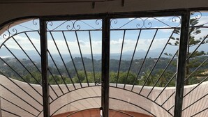 Un balcó amb barana corba, taula de vidre i vista a un paisatge de muntanya.