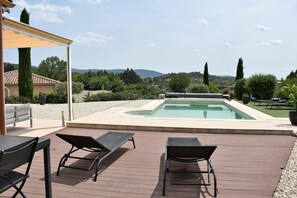 Ett poolområde med solstolar, en pergola och utsikt över det omgivande landskapet.