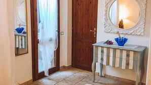 A room with a wooden door, a mirror, a small table with a vase, and a bed.