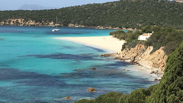 A coastal landscape with a sandy beach, clear turquoise waters, and a boat in the distance.