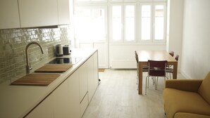 Ett modernt kök med en diskho, brödrost och en bänkskiva i trä. I det intilliggande vardagsrummet finns ett matbord med stolar och en soffa.