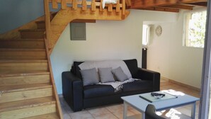 A living room with a black sofa, a small table, and a wooden staircase.