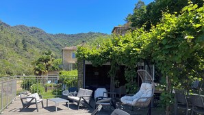 A wooden deck with outdoor furniture, including chairs and a table, overlooking a mountainous landscape.