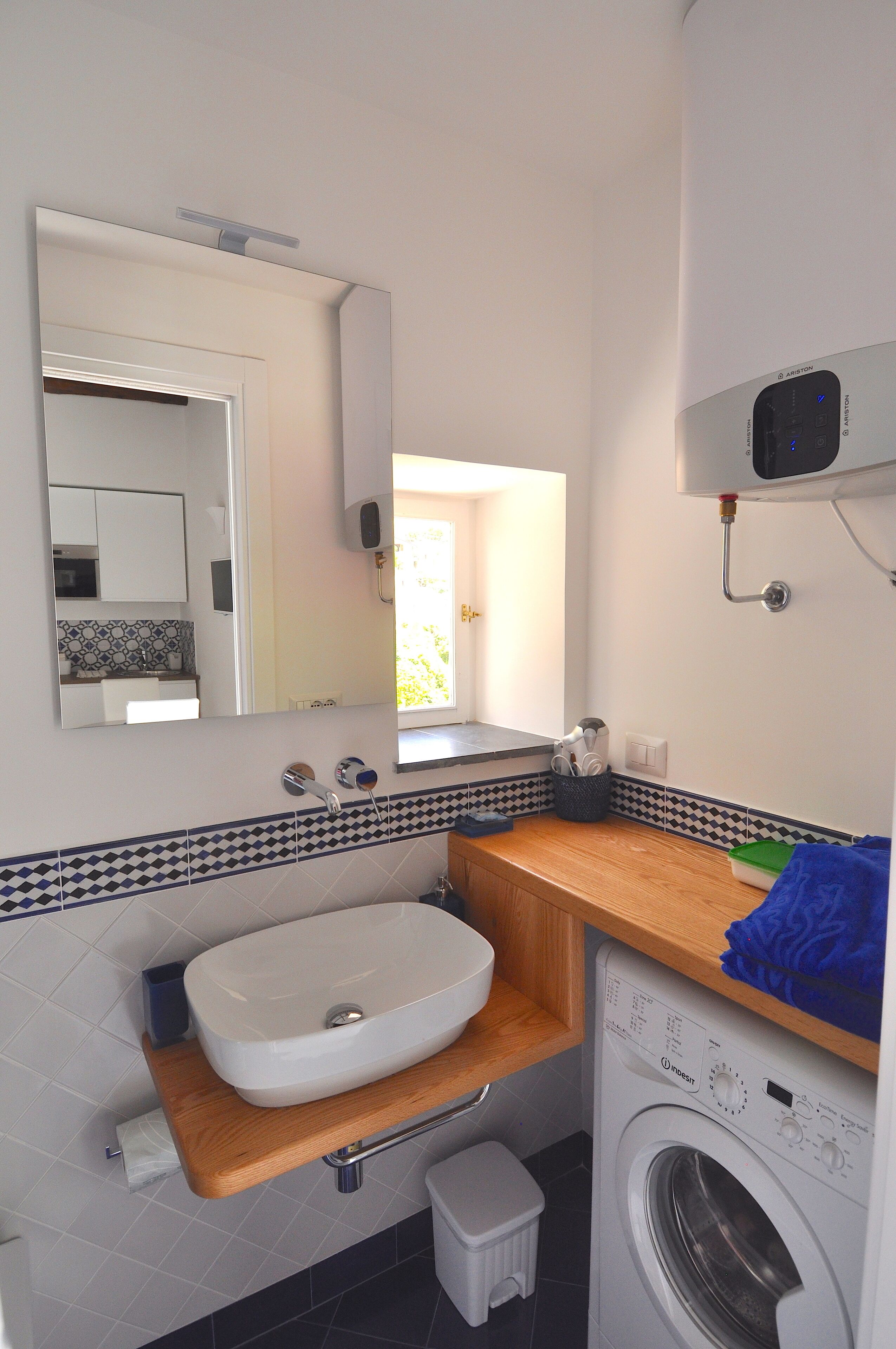 A compact bathroom with a sink, mirror, washing machine, and a small step stool.