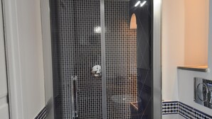 Una ducha a ras de suelo con mampara de vidrio, paredes con azulejos y un inodoro blanco visible a la derecha.