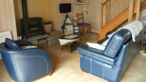 A cozy living room with a fireplace, two blue leather chairs, a wooden staircase, and a painting on the wall. - Penmarch: Country Cottage / Gite - Penmarc'h (Penmarch)