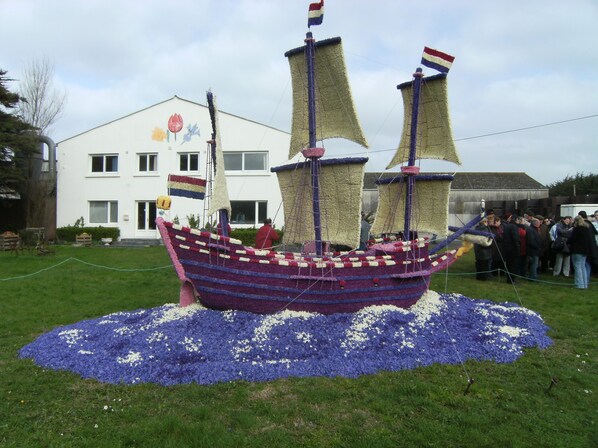 A ship-shaped flower arrangement in a grassy area with a building in the background.