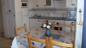 A kitchen with white cabinets, a microwave, a sink, and a dining table with chairs. - Penmarch: Country Cottage / Gite - Penmarc'h (Penmarch)