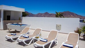 Zona de piscina con sillas de descanso y mesa de billar, rodeada por un muro blanco y vistas a la montaña.