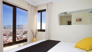 Habitación de hotel con cama, ventana grande con cortinas, balcón con sillones de descanso y espejo en la pared.