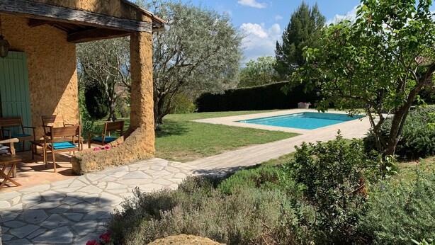 A pool area with a stone patio, wooden furniture, and a view of the surrounding garden. - Charming villa, heated swimming pool, 4 to 8 persons (Mormoiron)