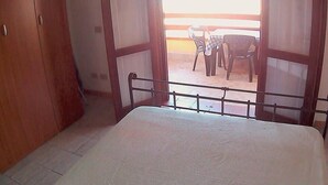 A bedroom with a bed, wooden wardrobe, and a balcony with plastic chairs. - TORRE DEI CORSARI, THE PEARL OF THE GREEN COAST - IUN Code: P7053 (Arbus)